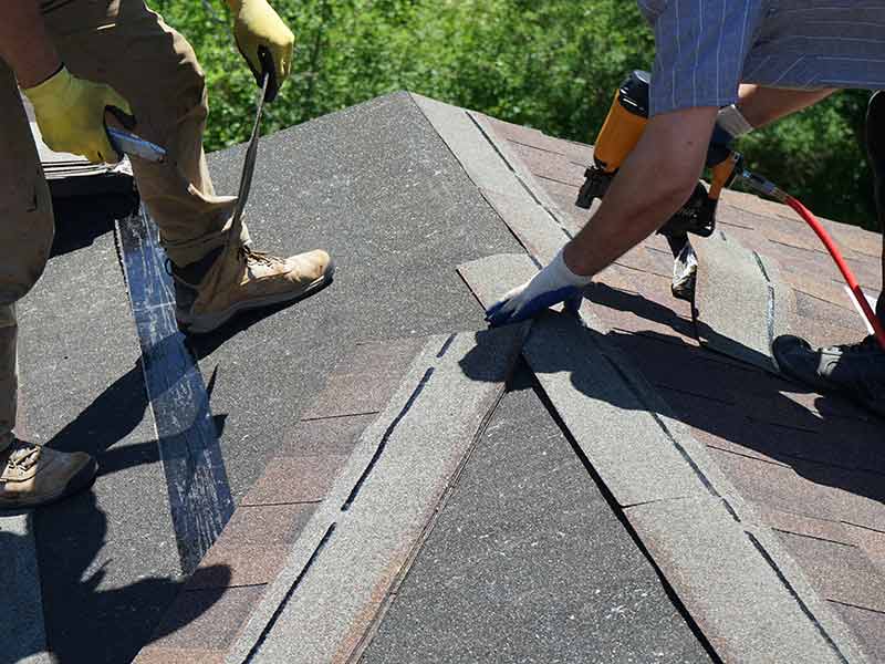 Close up of two workers installing new asphalt shingles on a residential roof